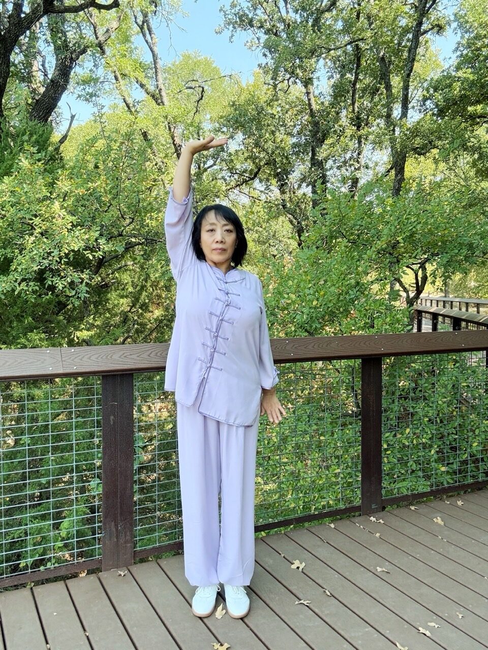 Vicki Zhao demonstrating a Qigong stretch in a lavender uniform on a boardwalk