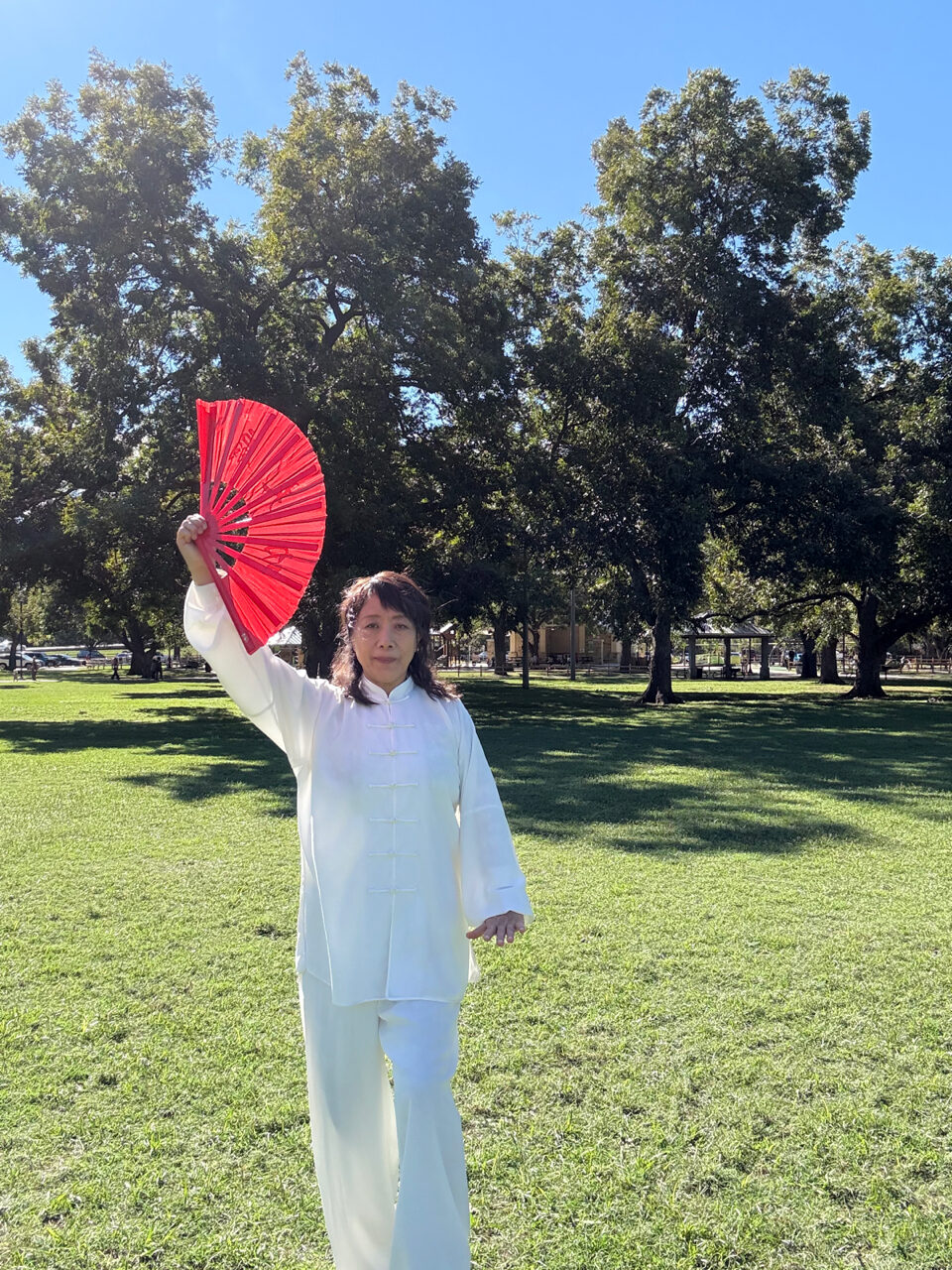 Vicki Zhao demonstrating a Tai Chi pose with a red fan in a park